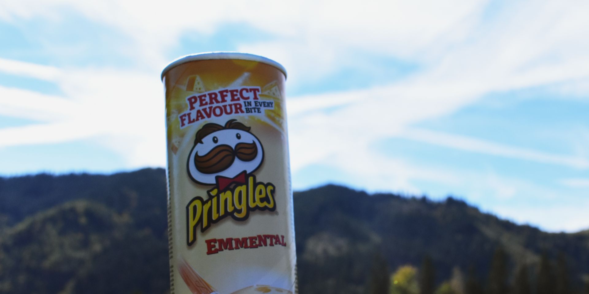 A can of Pringles is held up against a hillside.