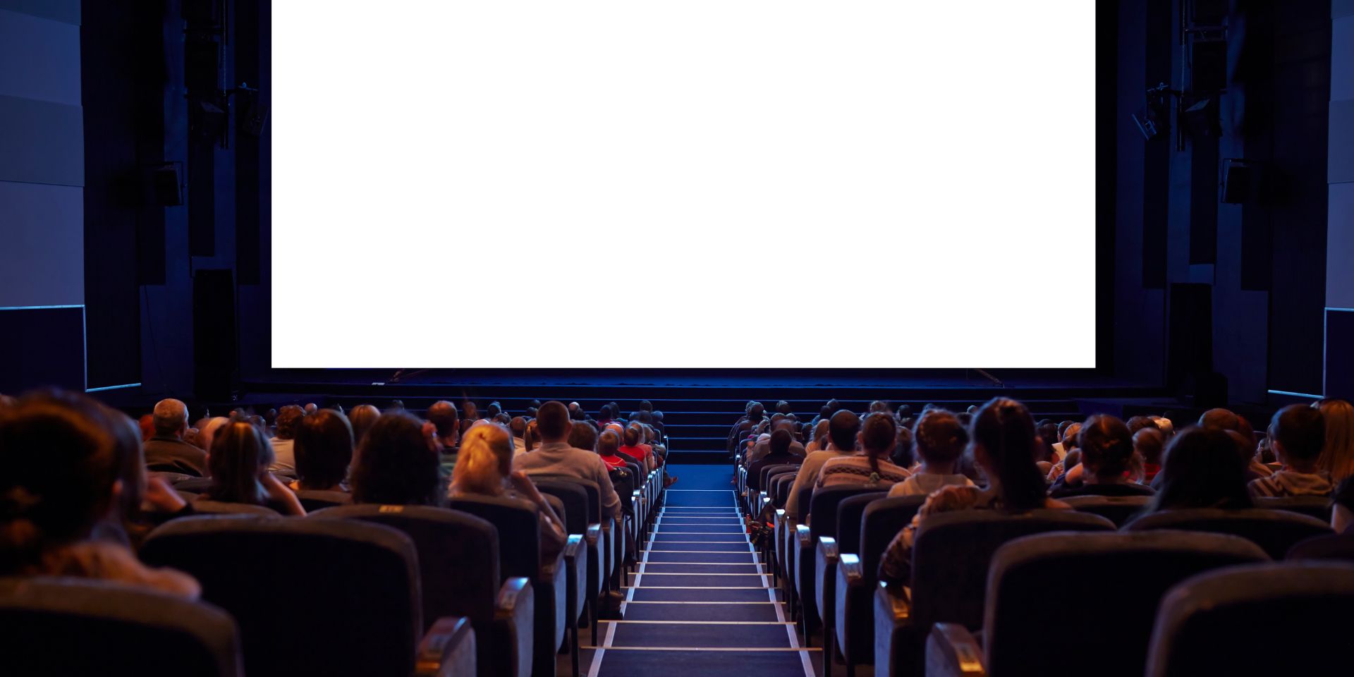 A group of conference attendees are seated, waiting for the on-stage talk to begin.
