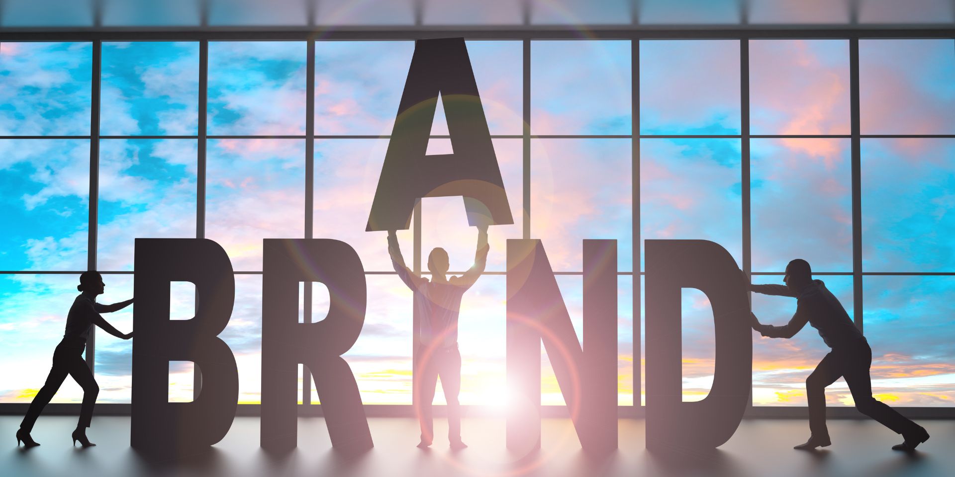 A man holds up the letter 'A' in the word 'Brand'. He is stood in front of a window with the sun behind him.
