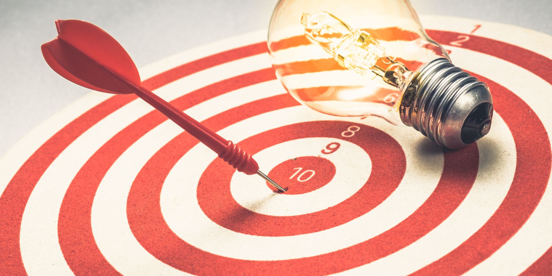 A red arrow is fixed to the centre of a red and white bullseye. A lightbulb sits to the right of the target.