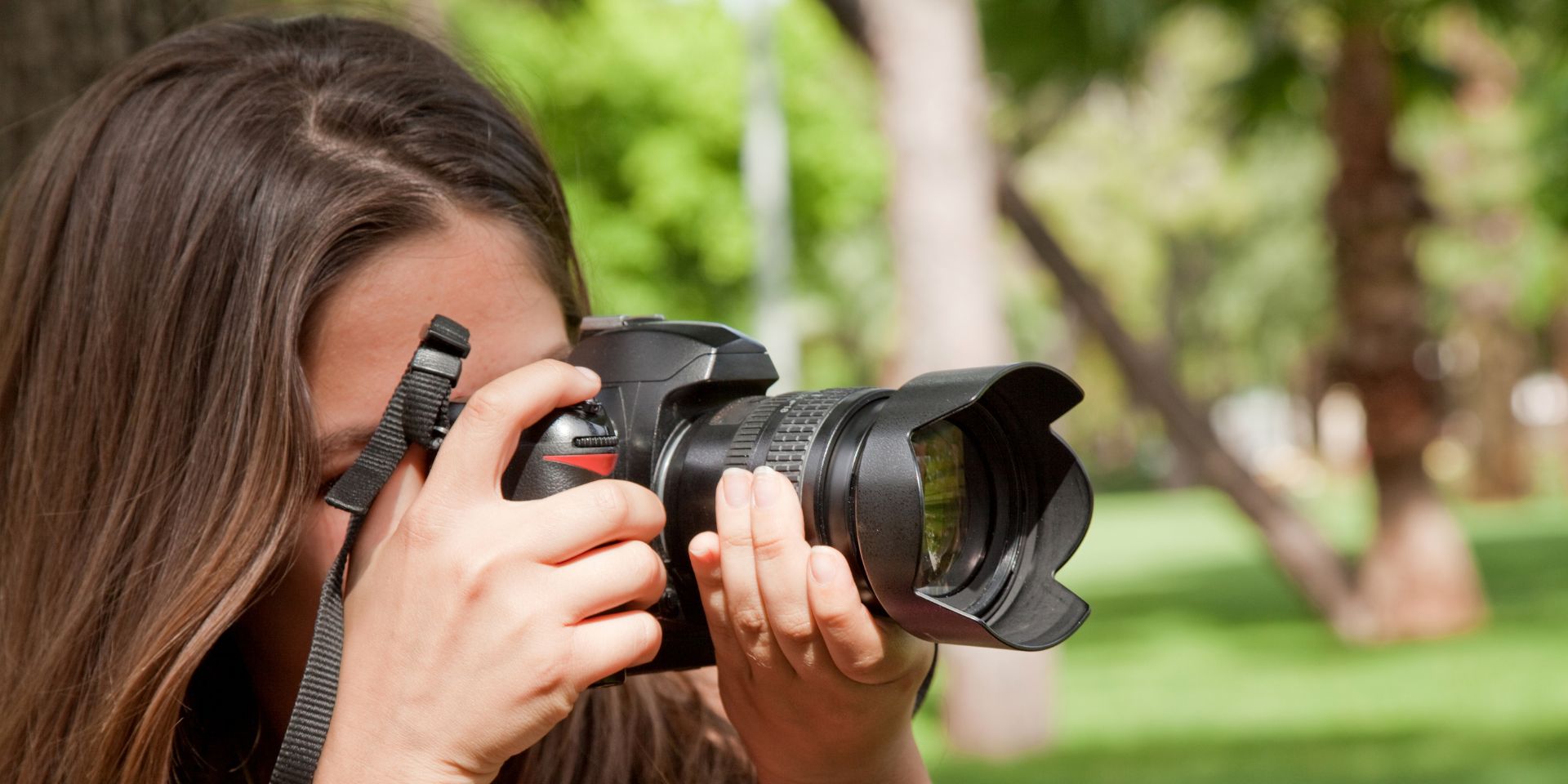 A close-up image of a female photographer shooting images for a social media profile, in a park.