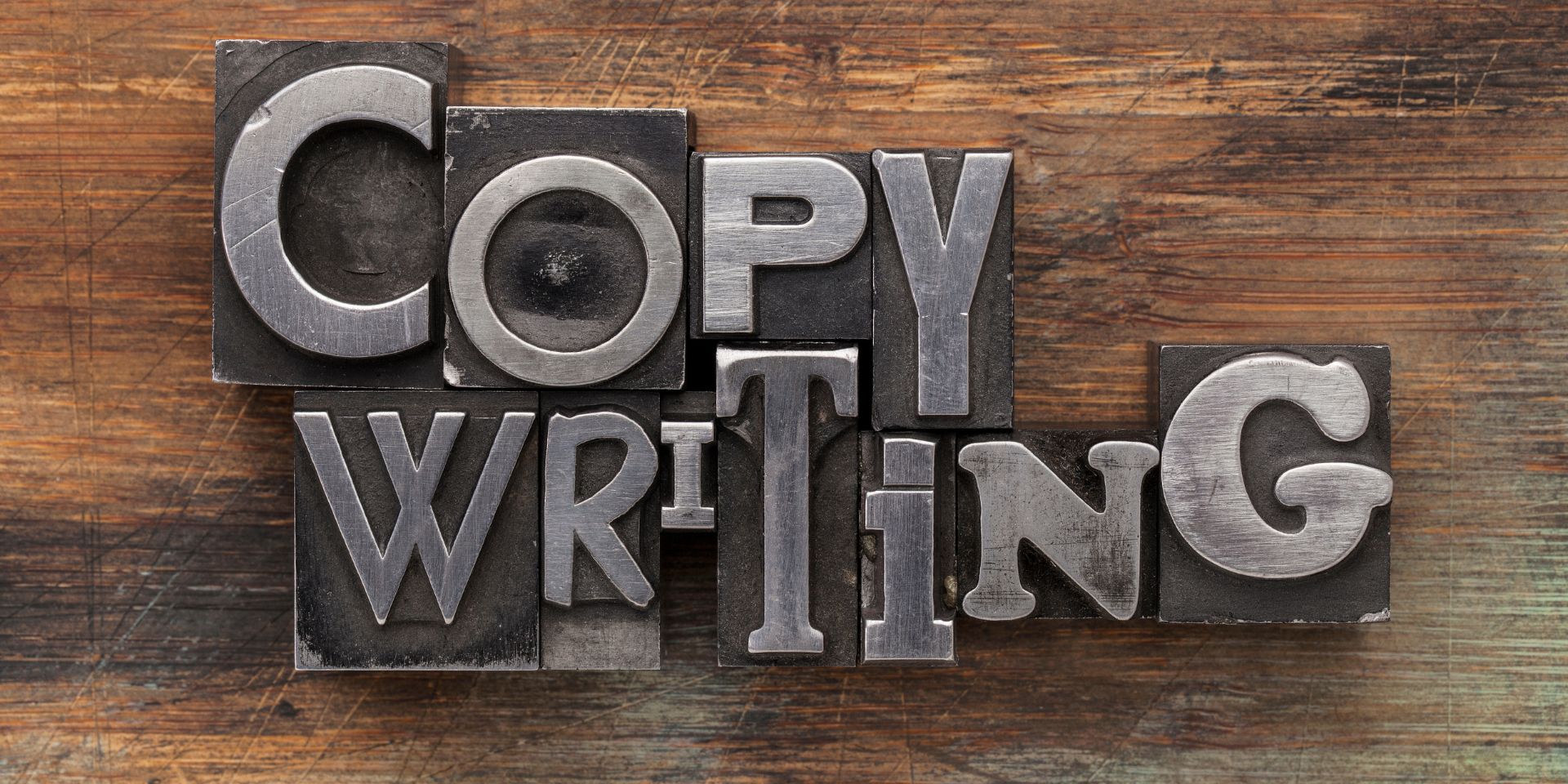 This image shows a metal printing press block with the word "Copywriting", shown against a wooden background.