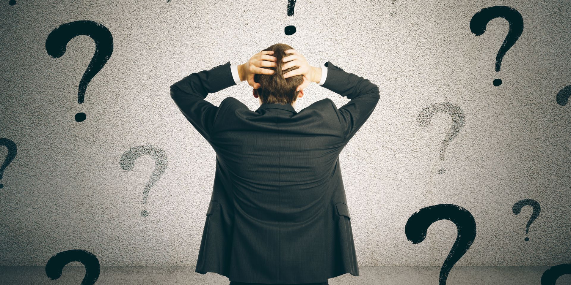 A businessman stands with his hands on his head, looking at the black question marks surrounding him.