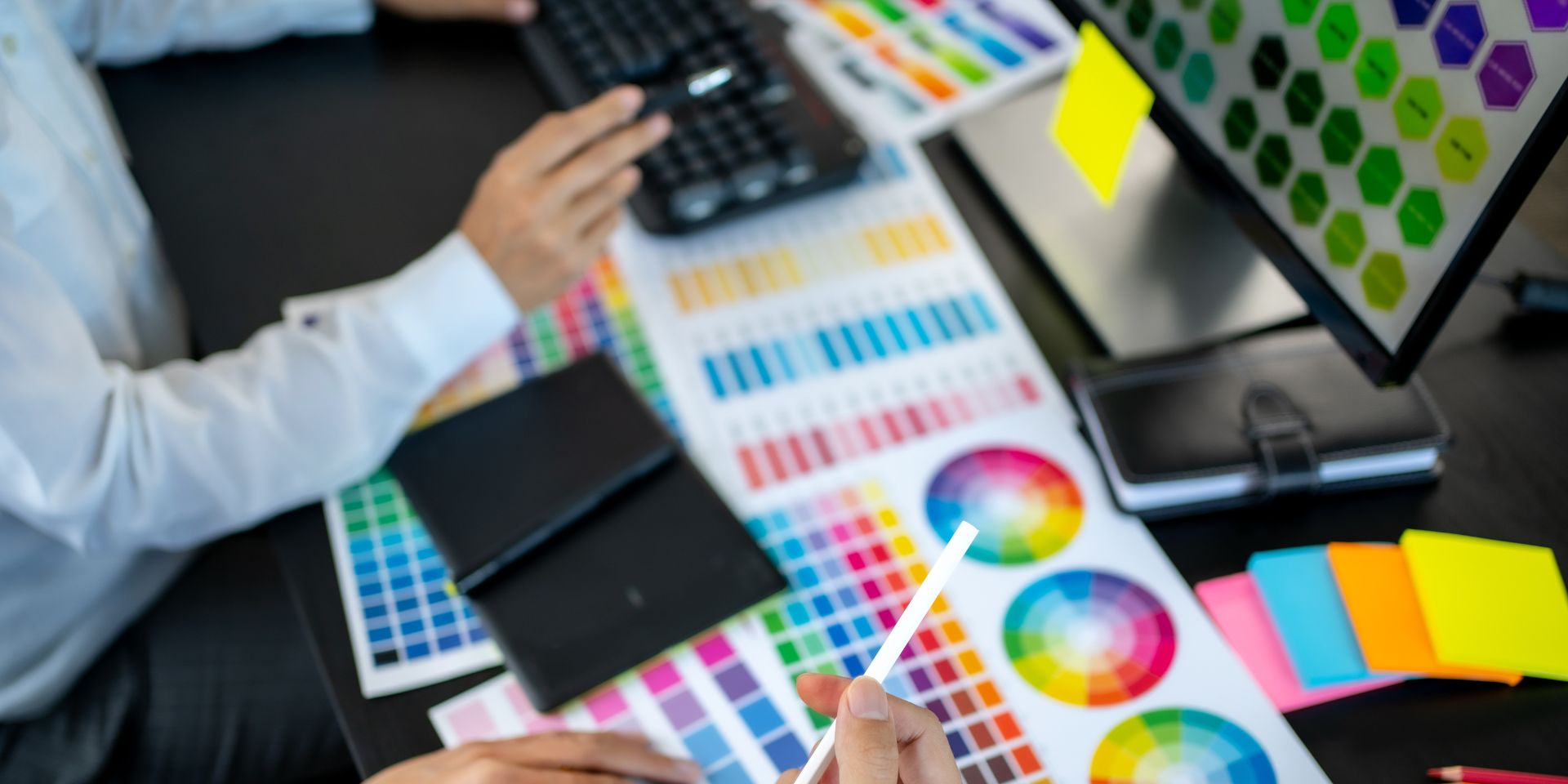 Web designers looking at hex codes on a computer monitor, that rests on a black office desk.
