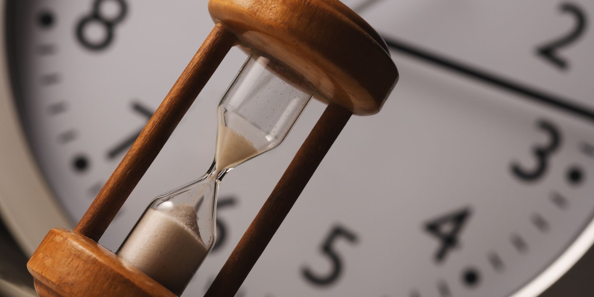 A black and white analogue wall clock appears in the background, with a wooden sand timer in the foreground.
