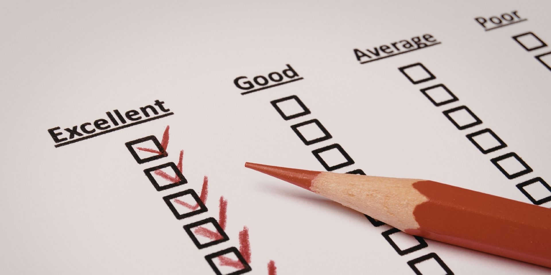 A column of black checkboxes under the heading "Excellent" has been ticked with a red pencil that's resting on the top of this sheet of paper.